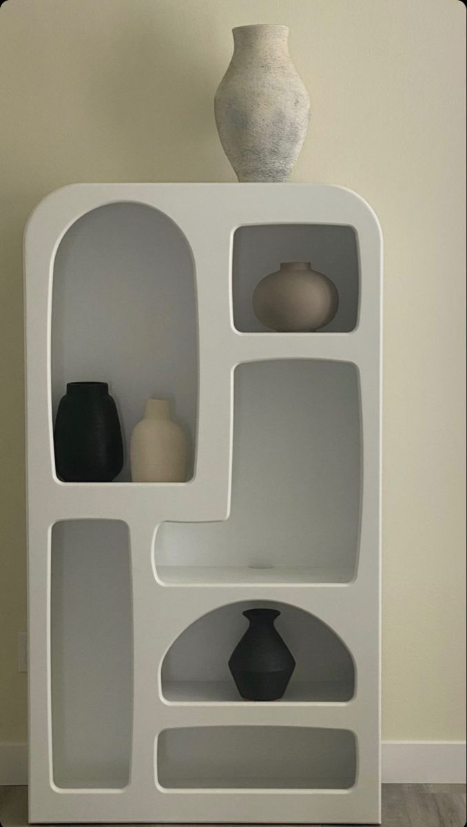 a white shelf with vases on top of it in front of a beige wall