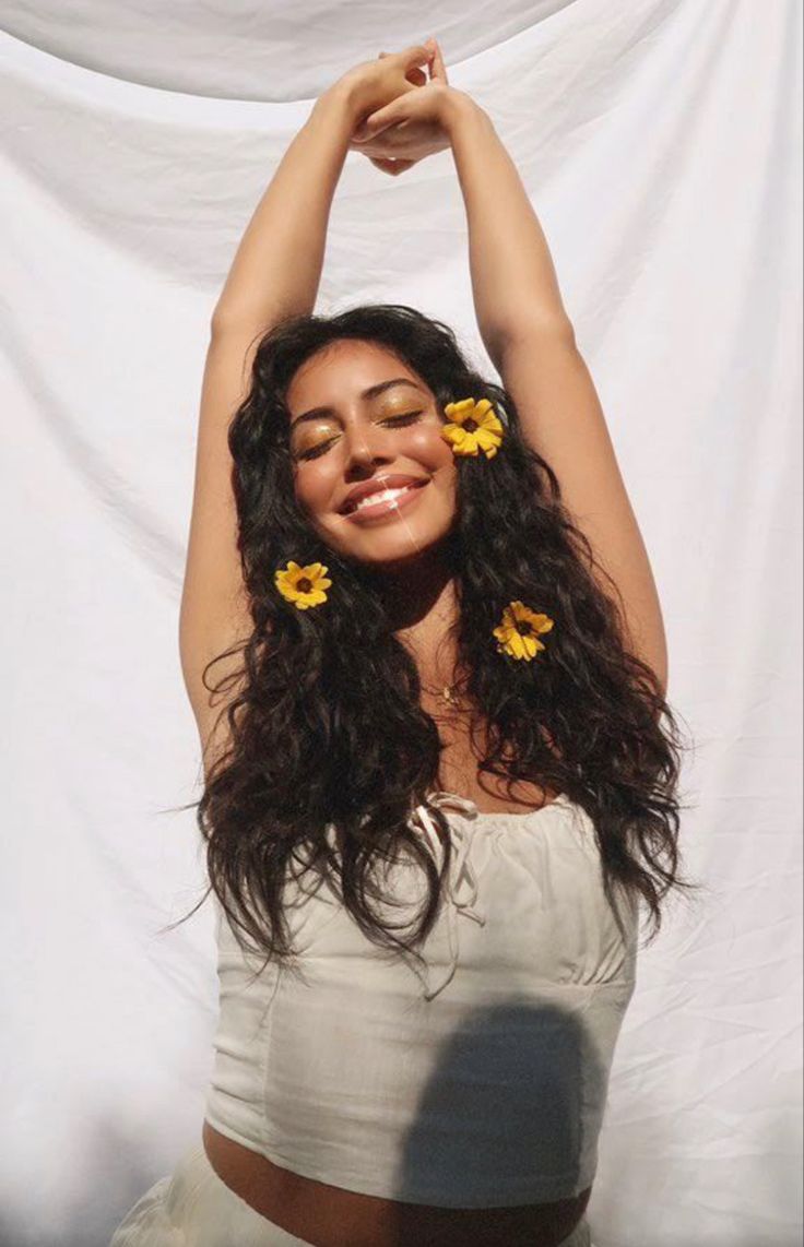 a woman with flowers in her hair standing next to a white sheet covered wall and smiling at the camera