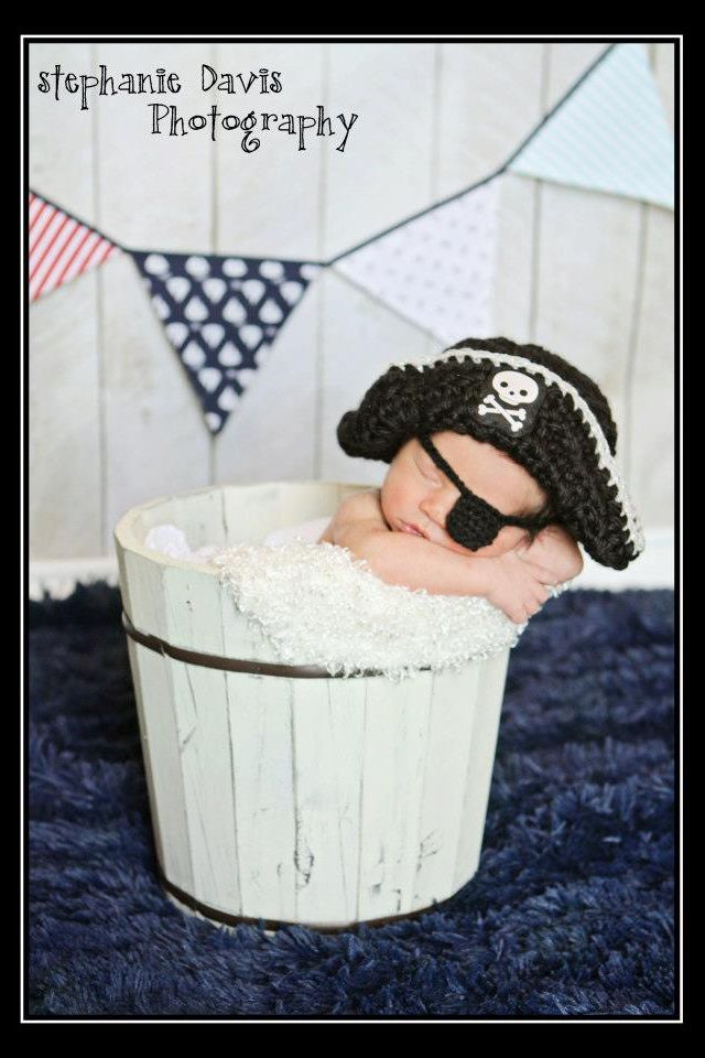 a baby is wearing a pirate hat while laying in a bucket with his head inside