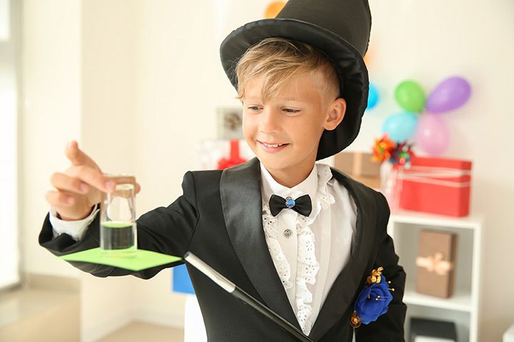 a young boy dressed in a black tuxedo and holding a beakle with green liquid