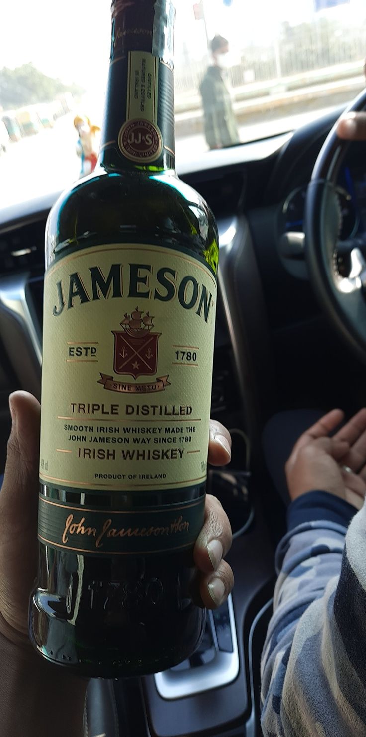 a person holding up a bottle of jameson in their hand while sitting in a car