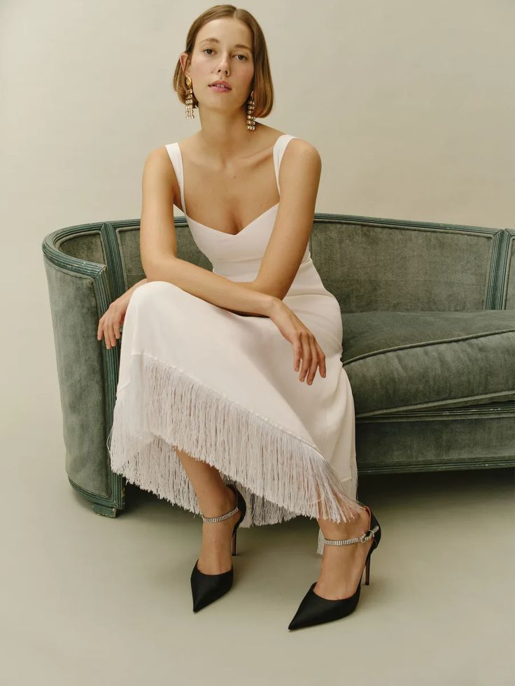 a woman sitting on top of a green couch next to a white wall and wearing high heels