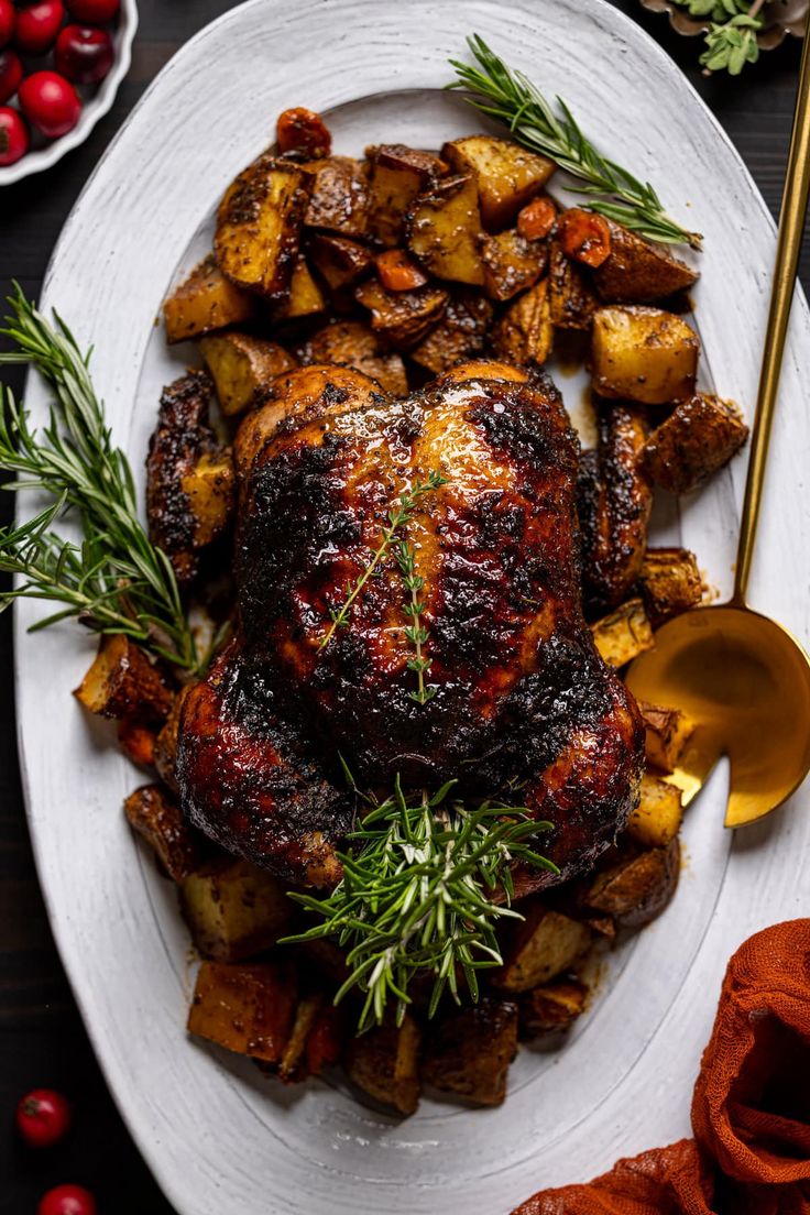 a roasted turkey with potatoes and herbs on a white plate next to a golden spoon