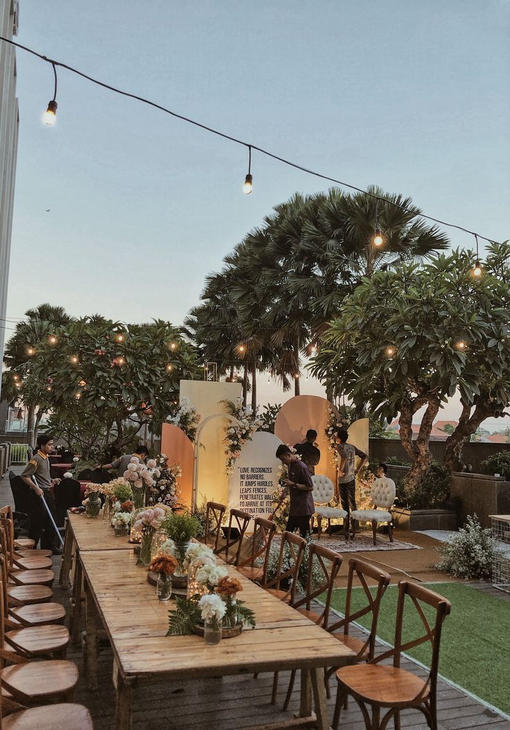 an outdoor dining area with wooden tables and chairs, surrounded by greenery and string lights