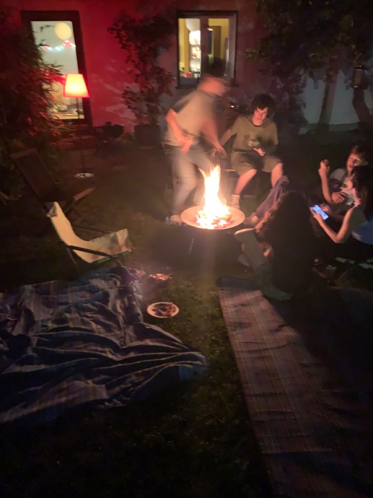 friends sitting around a fire on a late night in june, 2 picnic blankets in the foreground with an empty camping chair next to the fire Friends Driving At Night Aesthetic, Bbq Aesthetic Night, Family Barbeque Aesthetic, Night Picnic Aesthetic, Potluck Aesthetic, Late Night Party Aesthetic, Cookout Aesthetic, Late Night Picnic, Sahara Movie