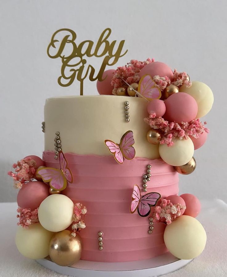 a baby girl cake with pink and white frosting, gold decorations and butterflies on top