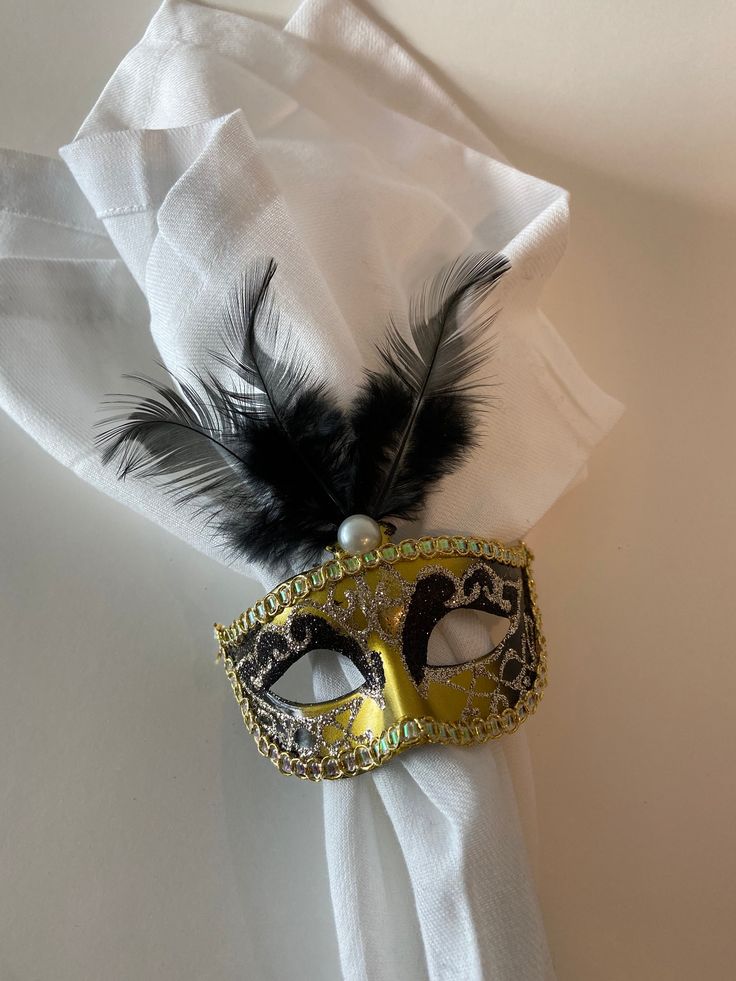 a masquerade mask with feathers on top of a white table cloth and napkin