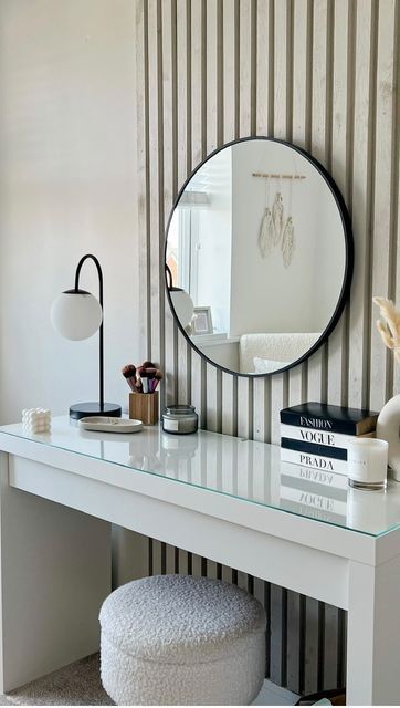 a white desk with a mirror, stool and books on top of it in front of a striped wall