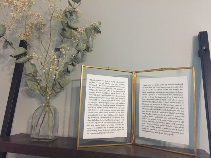 an open book sitting on top of a wooden shelf next to a vase with flowers