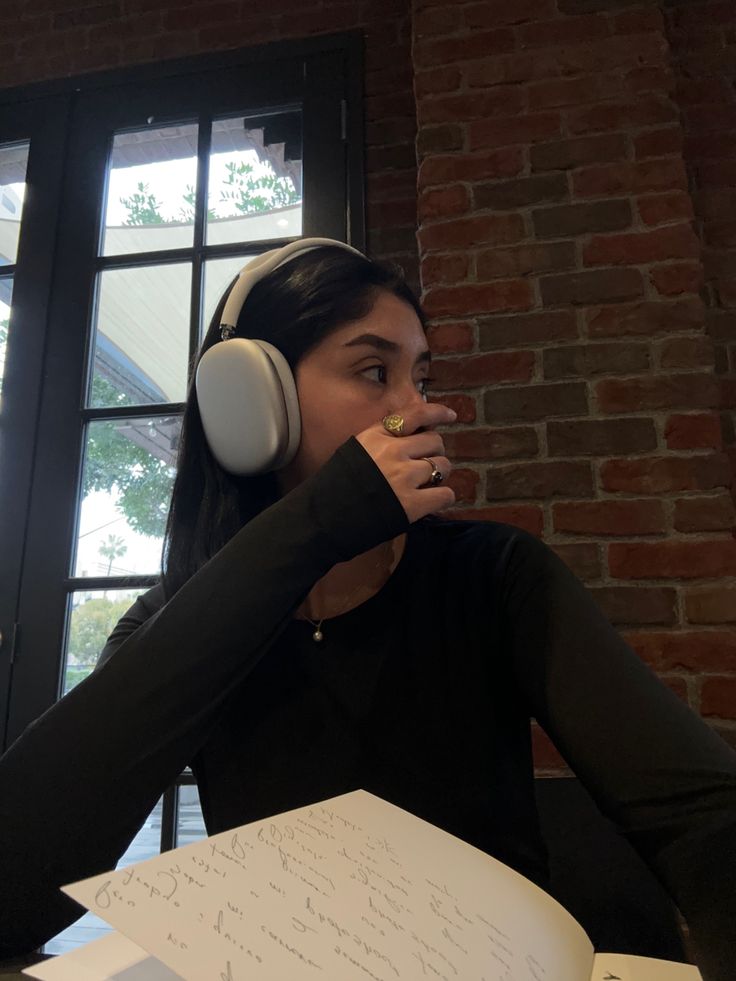 a woman sitting at a table with headphones on and writing in a note pad