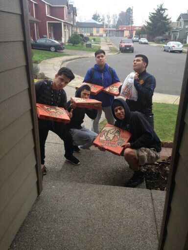 five people holding up pizza boxes in front of their faces on the steps to a house