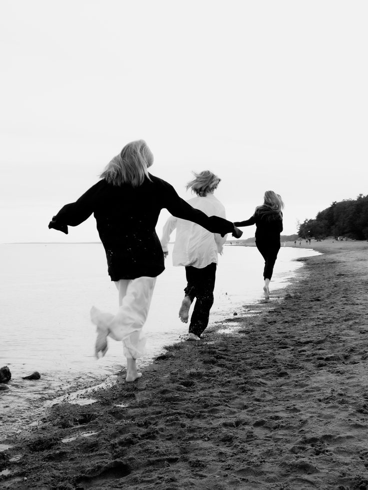 three people running on the beach holding hands with one person in black and white photo