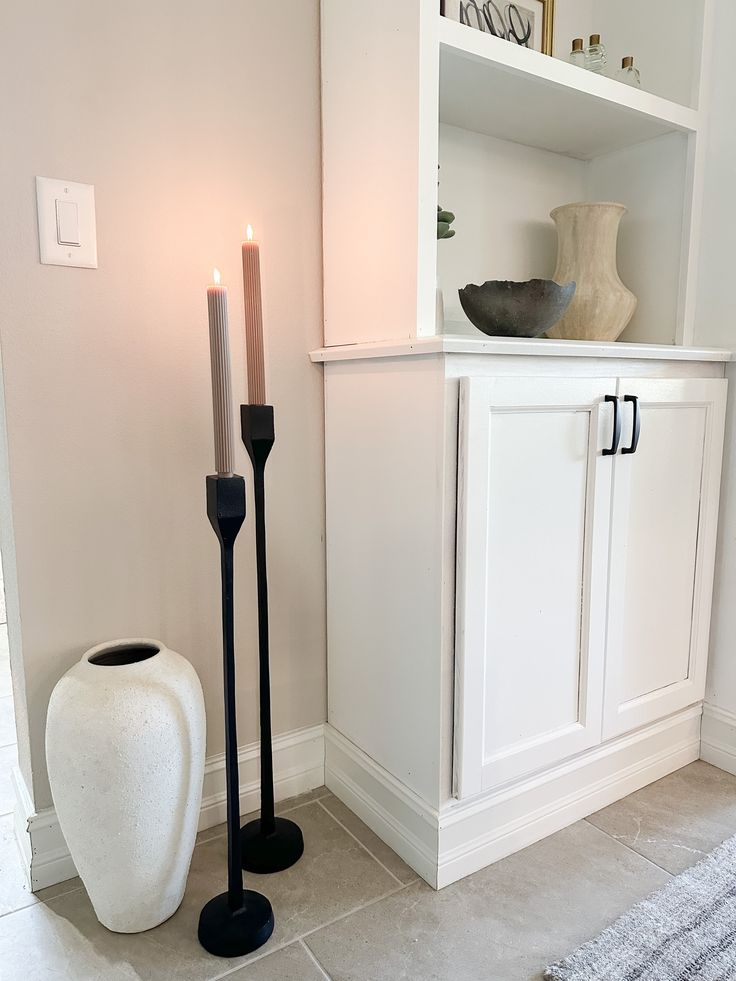 a white vase and two black candles in a room