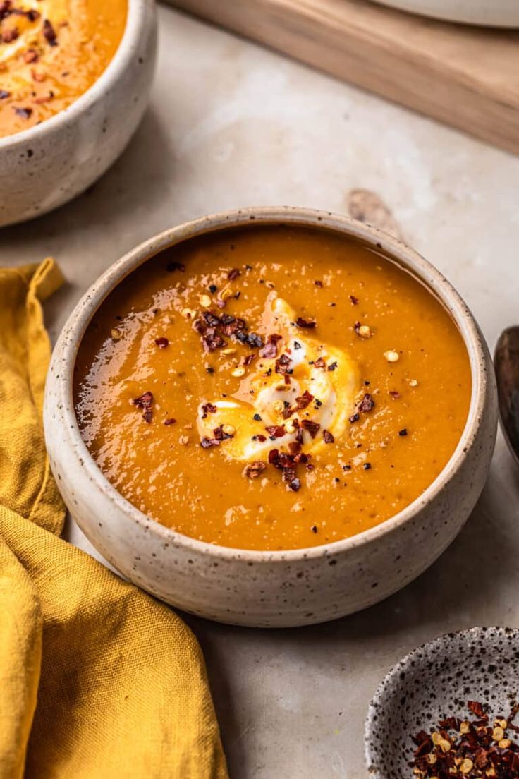 two bowls filled with carrot soup on top of a table