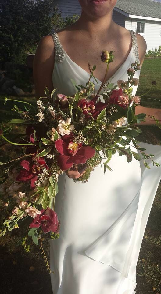 a woman in a white dress holding a bouquet of flowers and greenery on her wedding day