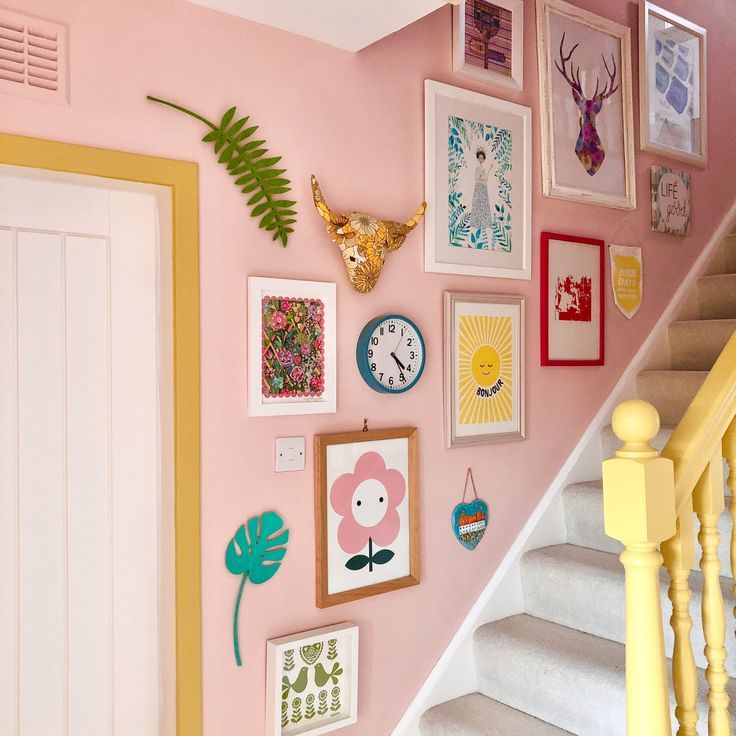 there are many framed pictures on the wall next to the stair case in this house