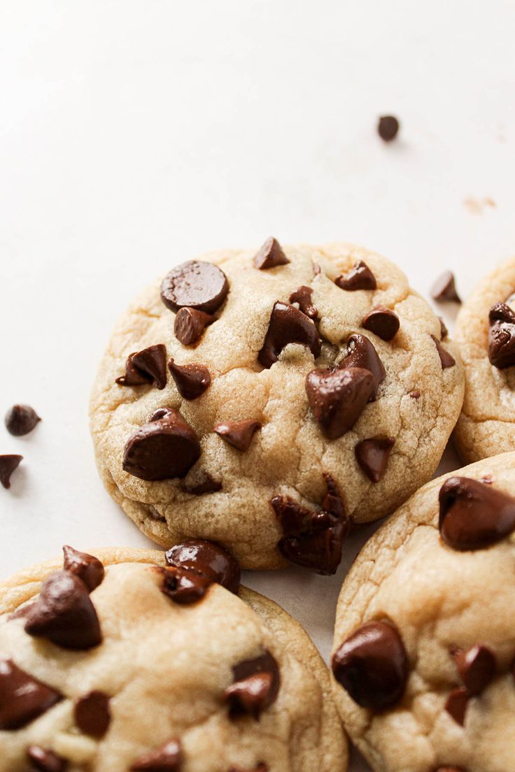 four chocolate chip cookies sitting on top of a white surface with scattered chocolate chips around them