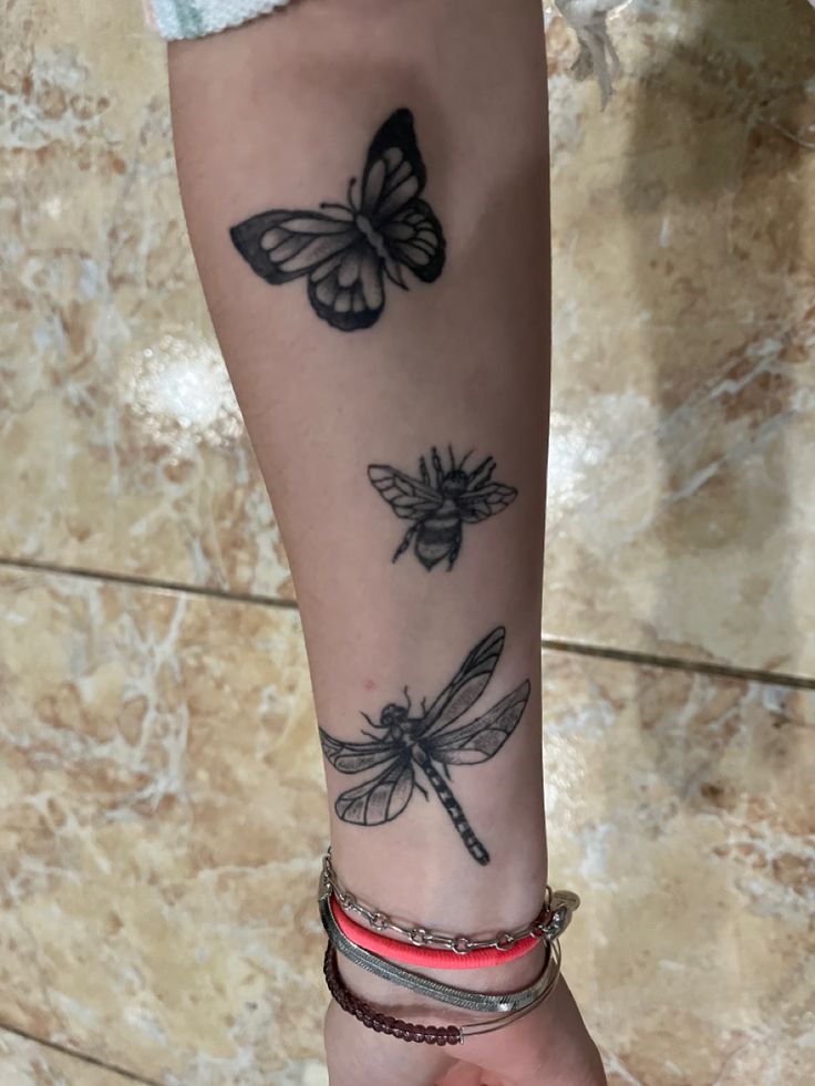 a woman's arm with tattoos on it and two dragonflys tattooed on the wrist