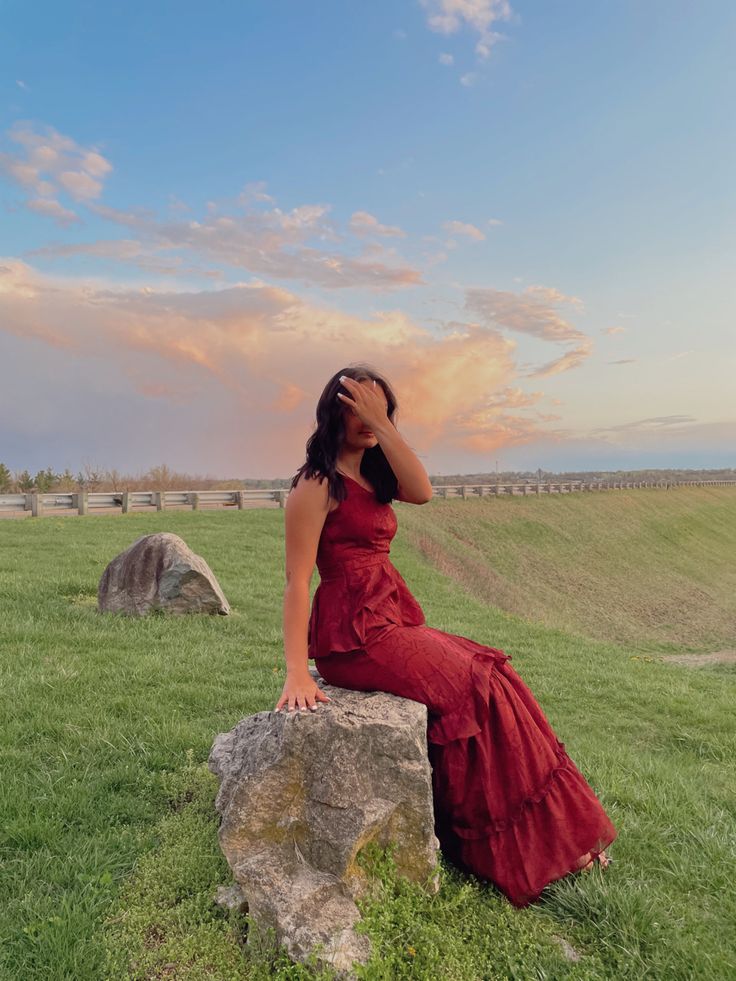 a woman in a red dress is sitting on a rock and looking into the distance