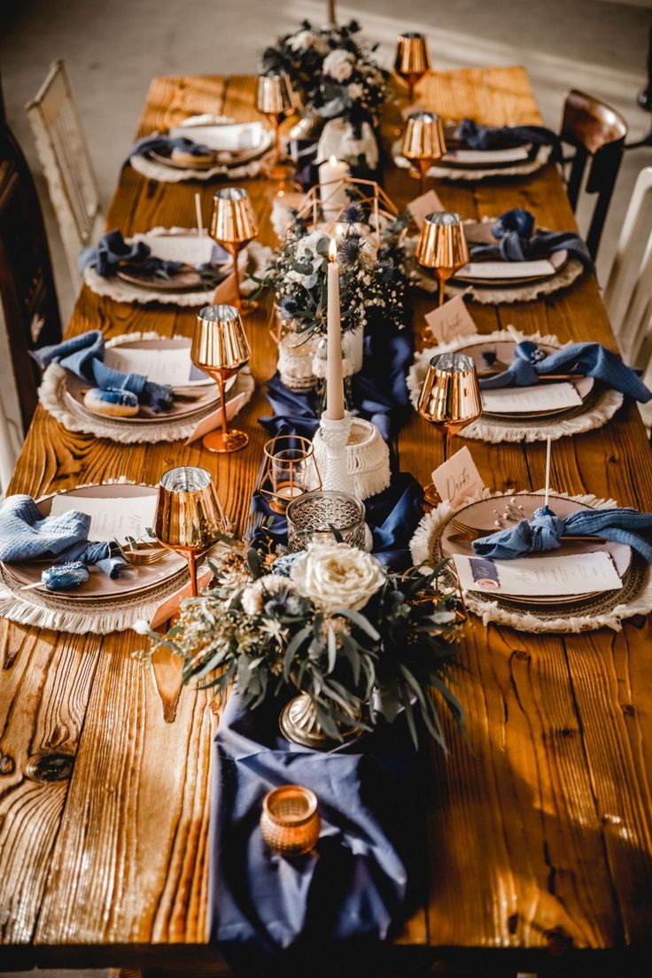 a wooden table topped with lots of plates and place settings covered in blue napkins