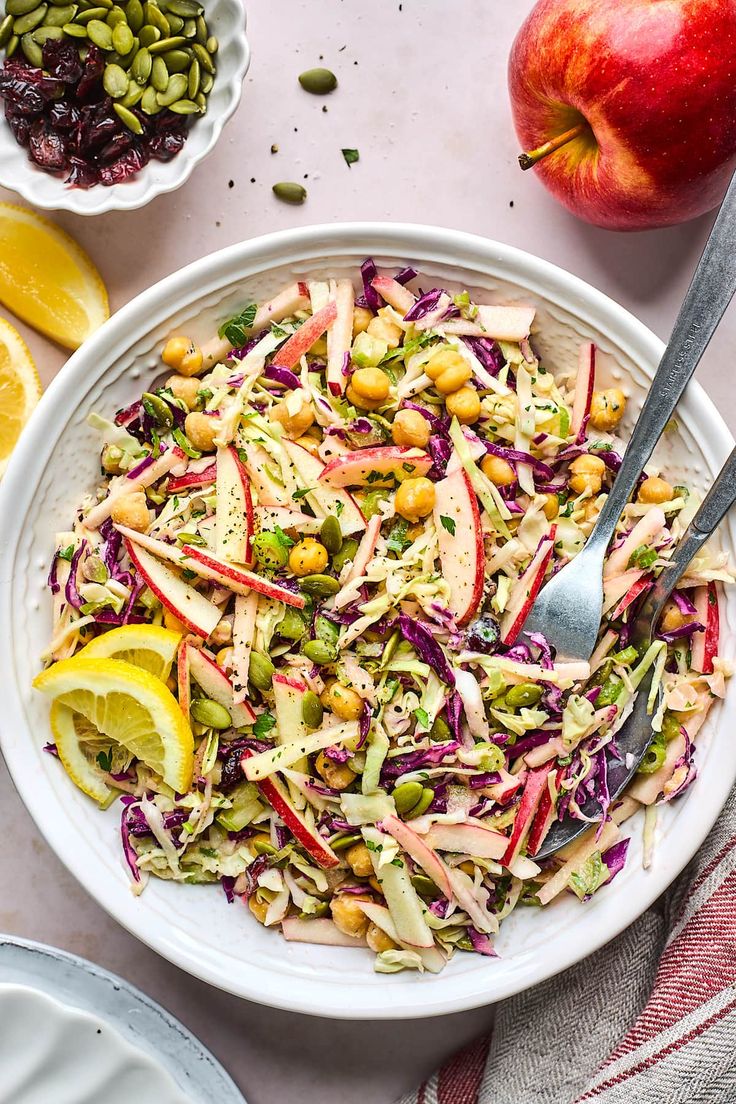 a white bowl filled with salad next to an apple and lemon wedges on top of a table