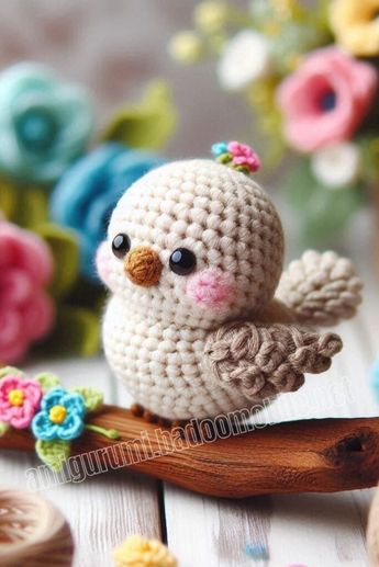 a small crocheted bird sitting on top of a wooden branch next to flowers