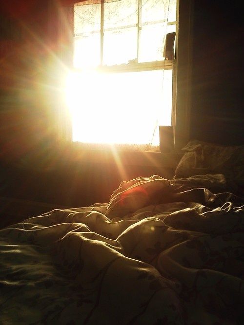 the sun is shining through an open window onto a bed with sheets and blankets on it