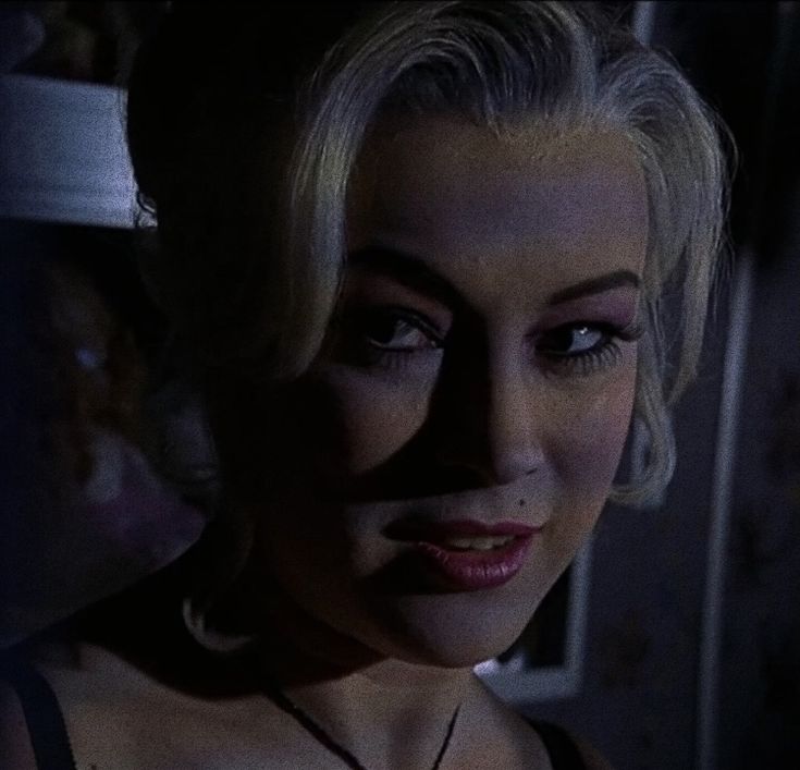 a close up of a woman with dark makeup and blonde hair in a dimly lit room