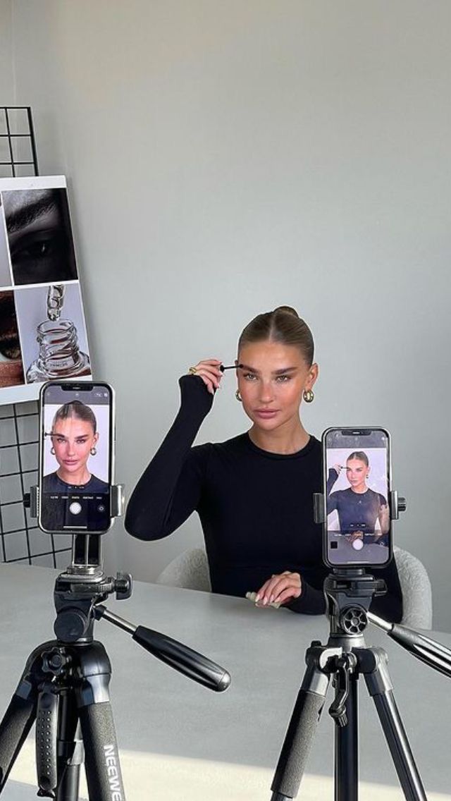 a woman sitting at a table with two cell phones in front of her and another person taking pictures