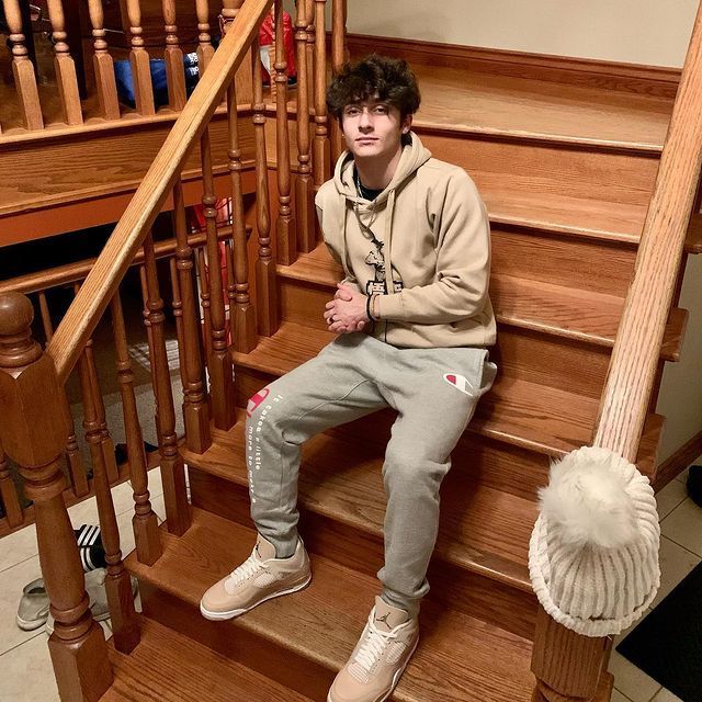 a young man sitting on top of a wooden stair case next to a banister