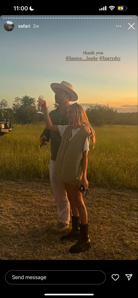 a man and woman standing next to each other in a field with the sun setting behind them