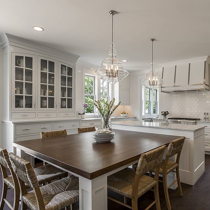 a large kitchen with white cabinets and wooden table surrounded by chairs in front of an island