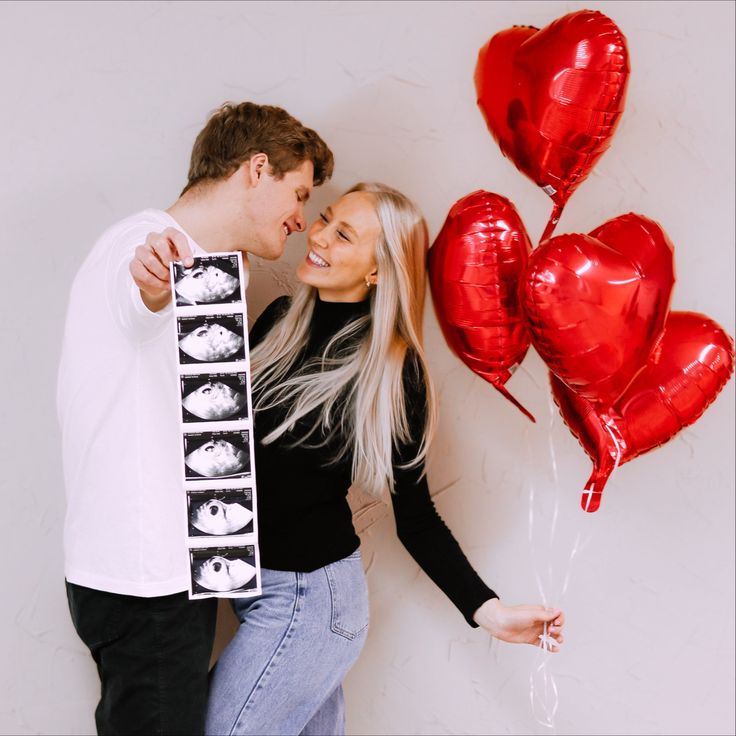 a man and woman standing next to each other with red balloons in front of them