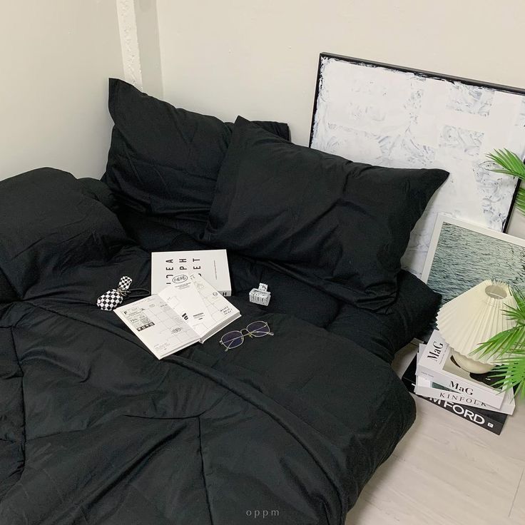 an unmade bed with black sheets and pillows on the floor next to a potted plant