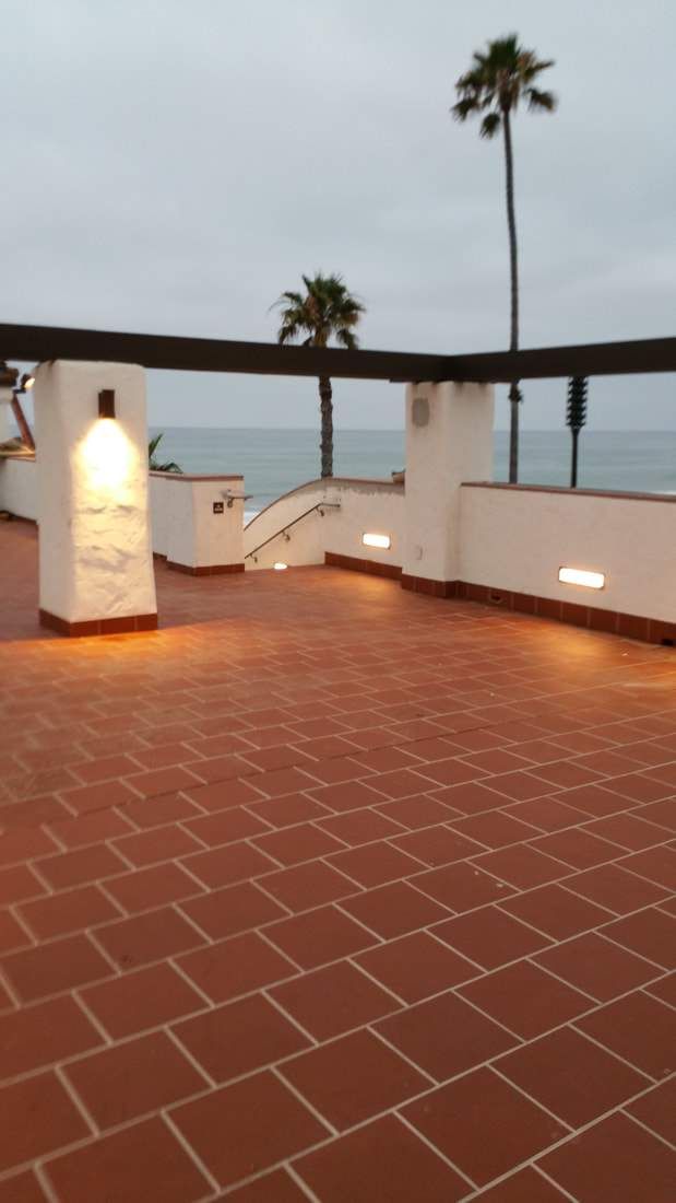 an empty patio with palm trees and lights on the wall next to the ocean in front of it