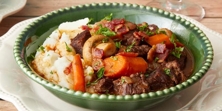 a green bowl filled with meat and veggies on top of a white plate