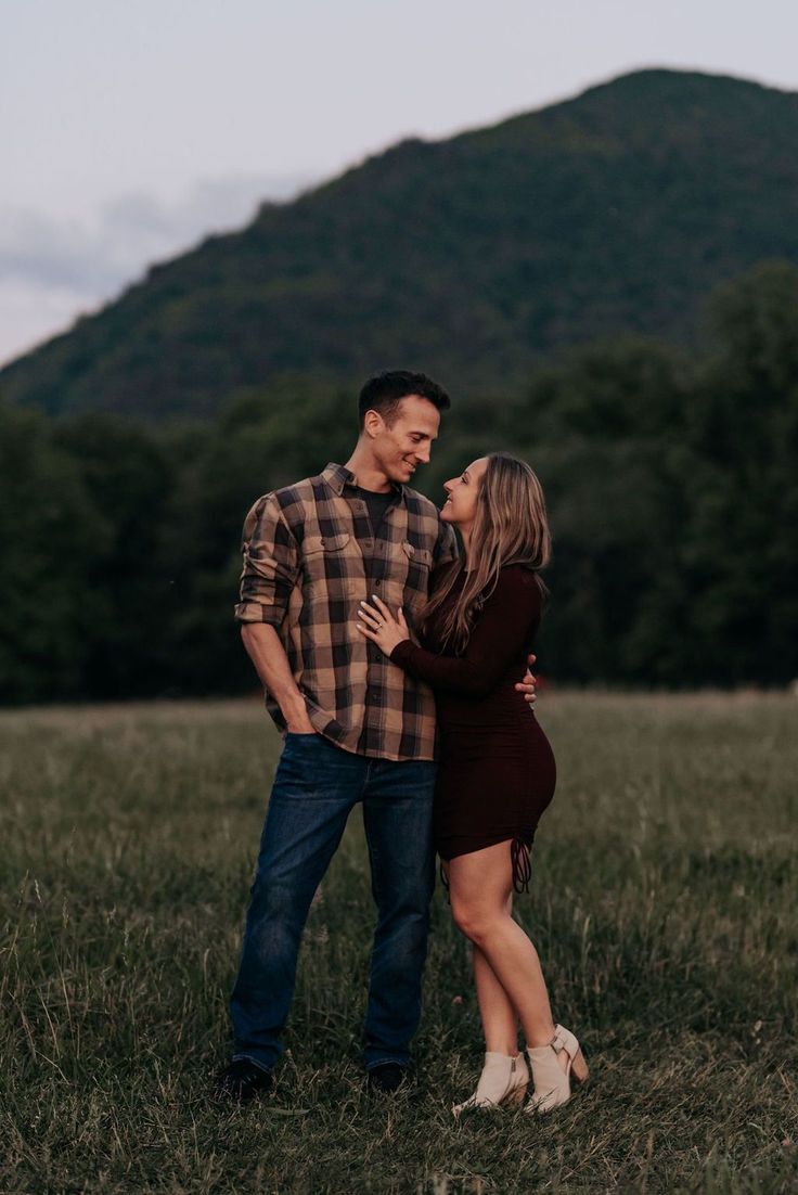 a man and woman are standing in the grass with their arms around each other as they look at each other