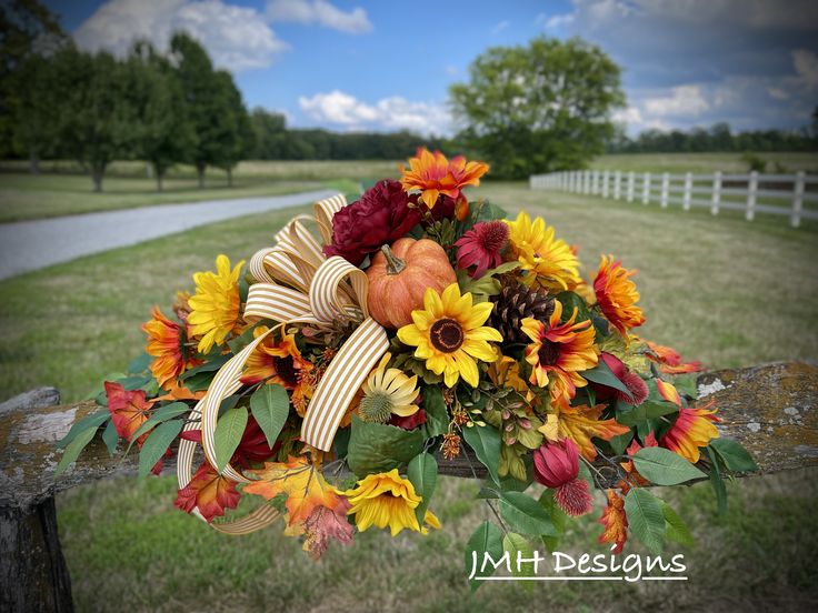 a bouquet of sunflowers, pumpkins and fall leaves on a fence post