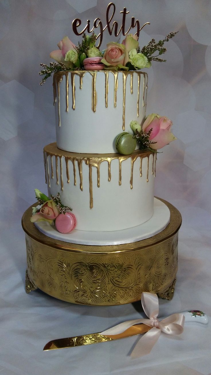 a three tiered cake with flowers and icing dripping down the side on a gold stand