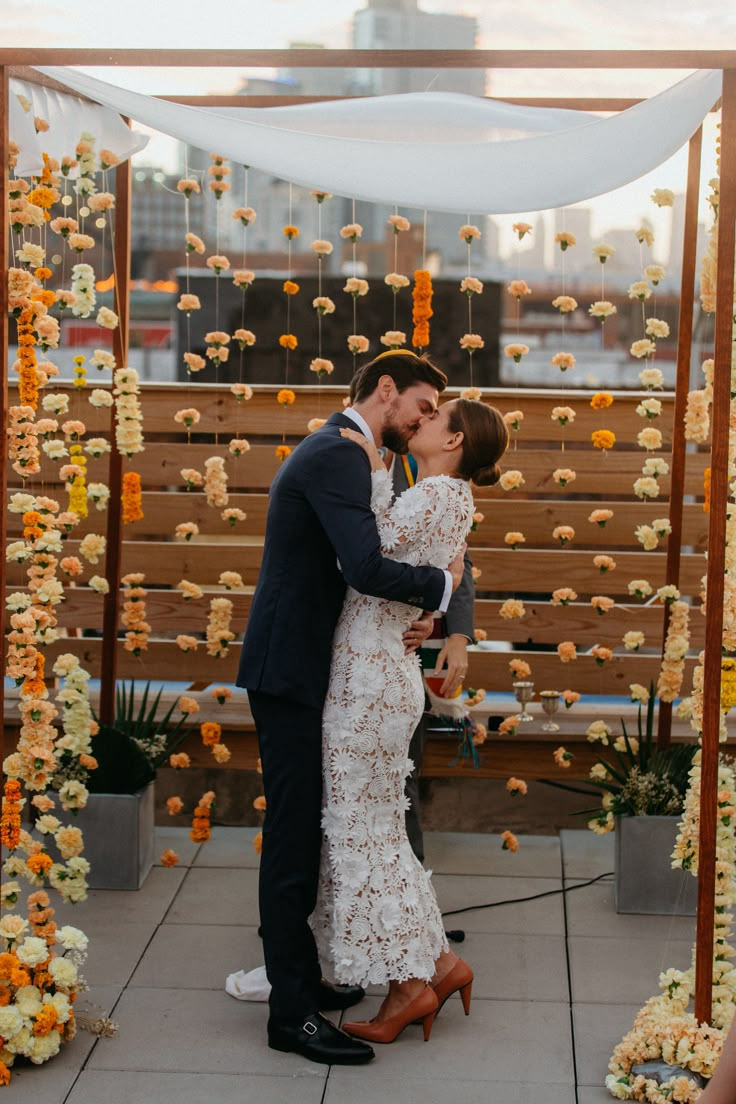 a bride and groom kissing in front of an outdoor ceremony arch with flowers on it