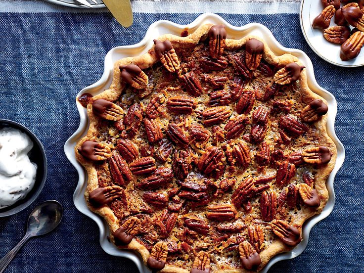 a pie with pecans in it on a blue tablecloth next to bowls of whipped cream and spoons