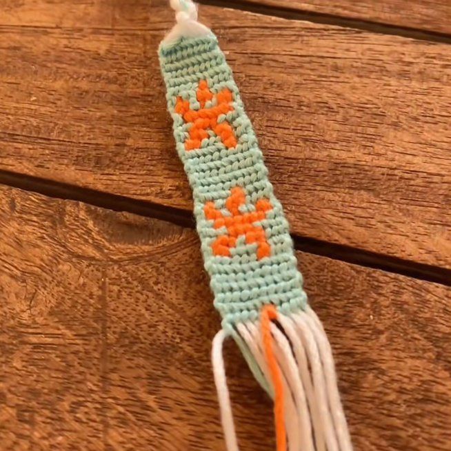 a crocheted bookmark with an orange flower on it sitting on top of a wooden table