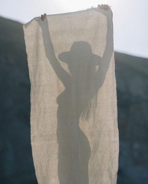 a woman in a hat and dress holding up a white towel with her shadow on it