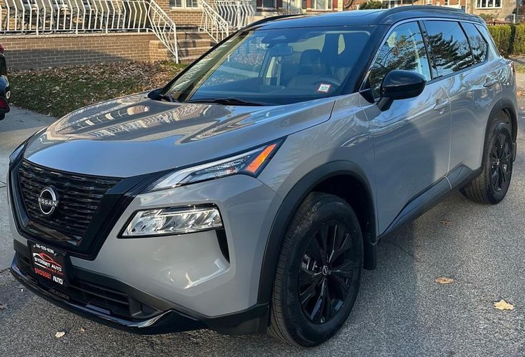 the front end of a silver nissan suv parked in a parking lot next to some houses