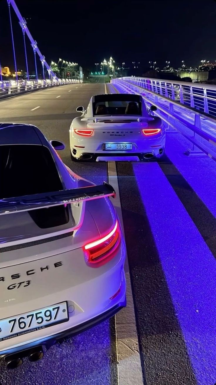 two cars parked on the side of a road at night with purple light coming from them