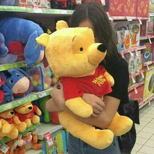 a woman holding a winnie the pooh stuffed animal in front of a store shelf