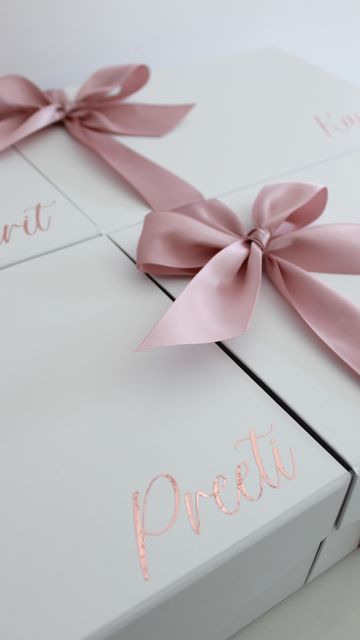 two white boxes with pink bows and the words pretti on them are wrapped in satin ribbon