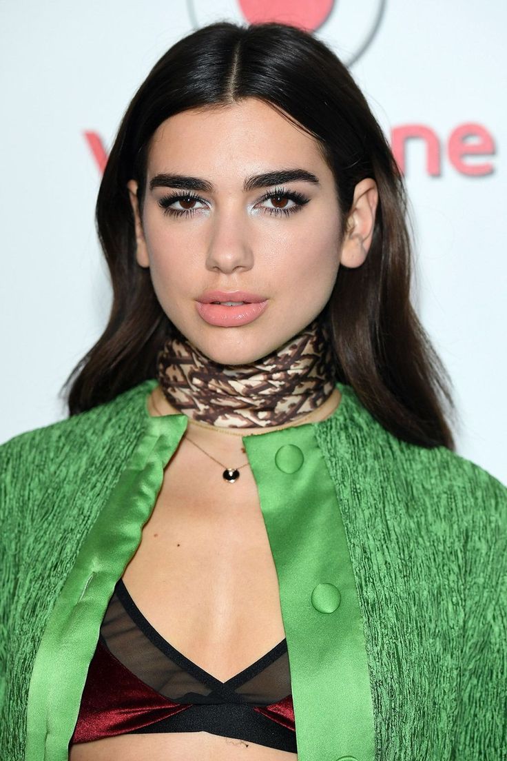 a woman with long hair wearing a green jacket and black bra top, posing for the camera