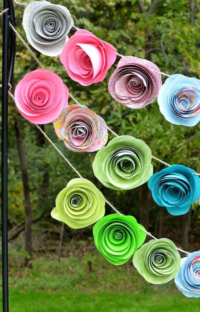 colorful paper flowers hanging from a clothes line in the grass with trees in the background