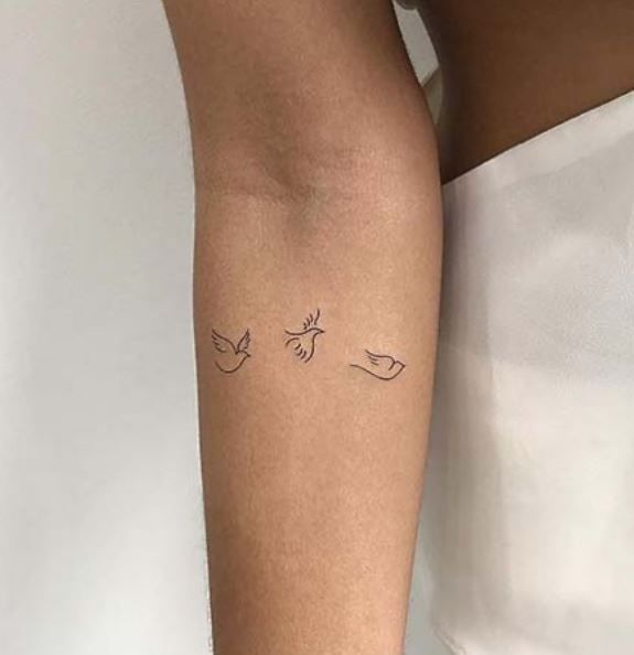 a woman's arm with two small birds on it, one is black and the other is white